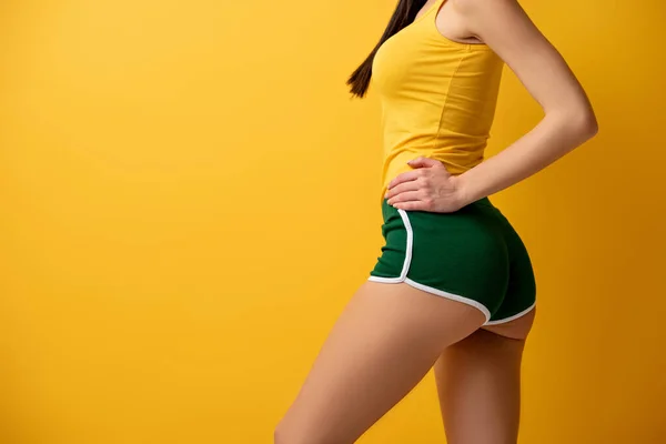 Vista recortada de chica delgada de pie en pantalones cortos verdes en amarillo - foto de stock