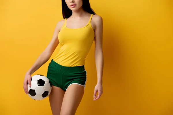 Cropped view of female football fan in shorts holding ball on yellow — Stock Photo