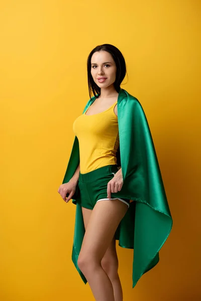 Beautiful female football fan in shorts holding brazilian flag on yellow — Stock Photo