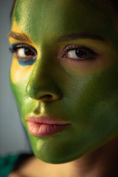 Female football fan with painted brazilian flag on face isolated on grey — Stock Photo