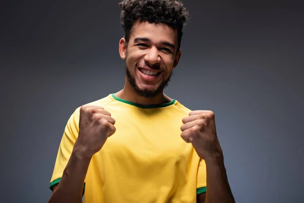 Fanático del fútbol americano africano feliz en camiseta amarilla gestos en gris - foto de stock