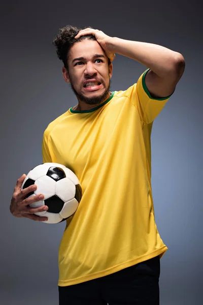 Gestresster afrikanisch-amerikanischer Fußballfan in gelbem T-Shirt mit Ball auf grau — Stockfoto