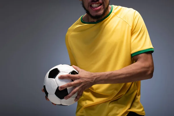 Cropped view of emotional football fan in yellow t-shirt holding ball on grey — Stock Photo