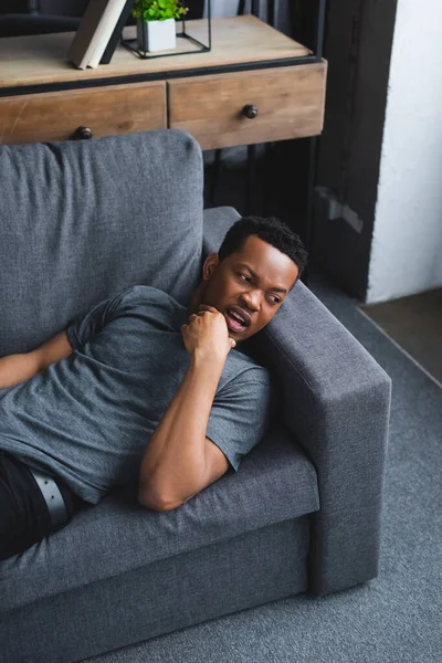 Preocupado hombre afroamericano acostado en el sofá en casa - foto de stock