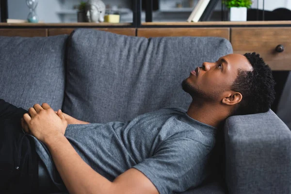 Homme afro-américain solitaire couché sur le canapé à la maison — Photo de stock