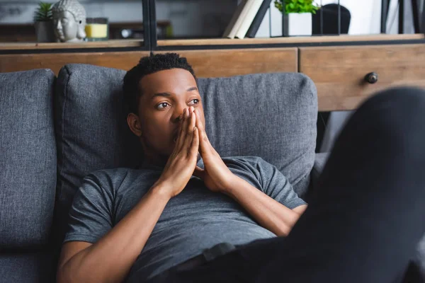 Sad thoughtful african american man lying on sofa at home — Stock Photo