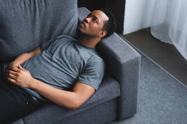 Одинокий грустный африканский американец, лежащий дома на диване — стоковое фото