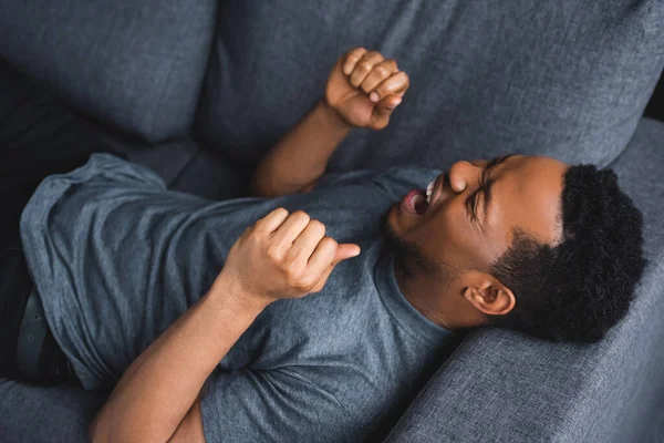 Homem afro-americano estressado gritando enquanto estava deitado no sofá em casa — Fotografia de Stock