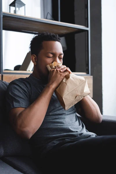 Worried african american man breathing with paper bag while having panic attack at home — Stock Photo