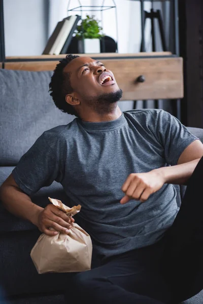 Gestresster afrikanisch-amerikanischer Mann hält Papiertüte bei Panikattacke zu Hause — Stockfoto