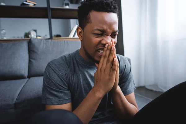 Stressed african american man with hands together suffering from panic attack at home — Stock Photo