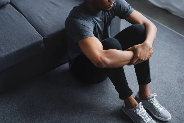 Cropped view of sad african american man sitting on floor at home — Stock Photo