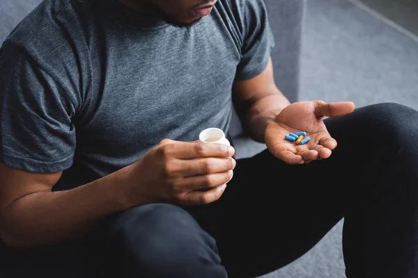 Vista recortada del hombre afroamericano tomando píldoras en casa - foto de stock