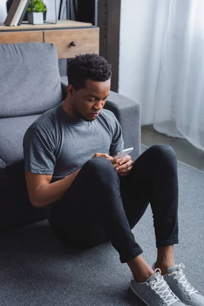 Triste homem americano africano usando smartphone em casa — Fotografia de Stock