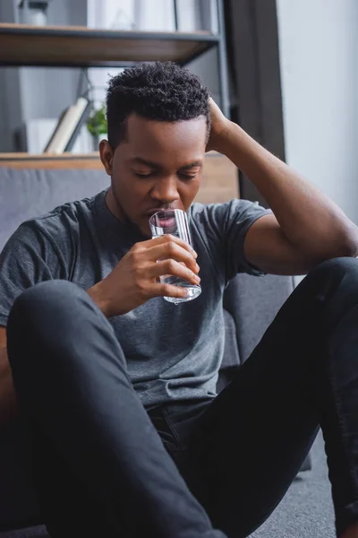 Estresado hombre afroamericano solitario beber agua en casa - foto de stock