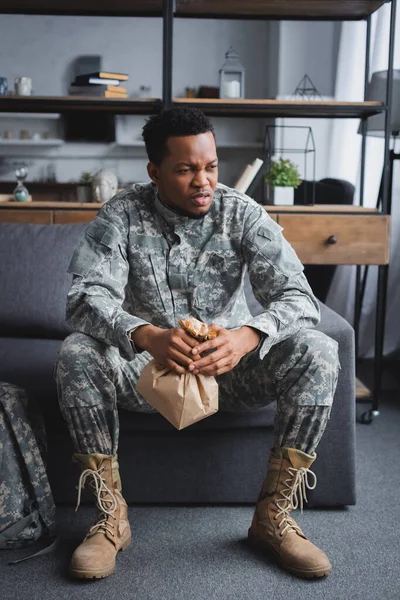 Soldat afro-américain en uniforme militaire tenant un sac en papier tout en ayant une attaque de panique et souffrant de stress post-traumatique à la maison — Photo de stock