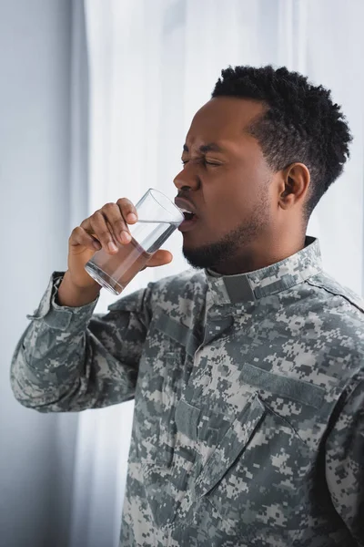 Stressed african american soldier drinking water and suffering from PTSD at home — Stock Photo