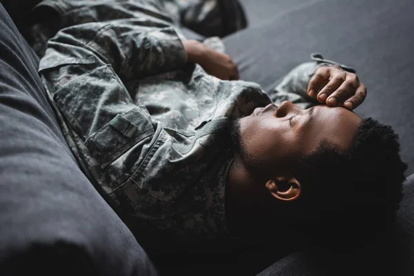 Cansado afroamericano soldado en uniforme militar durmiendo en sofá en casa - foto de stock