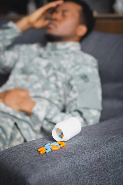 Selective focus of pills and tired african american soldier suffering from PTSD at home — Stock Photo