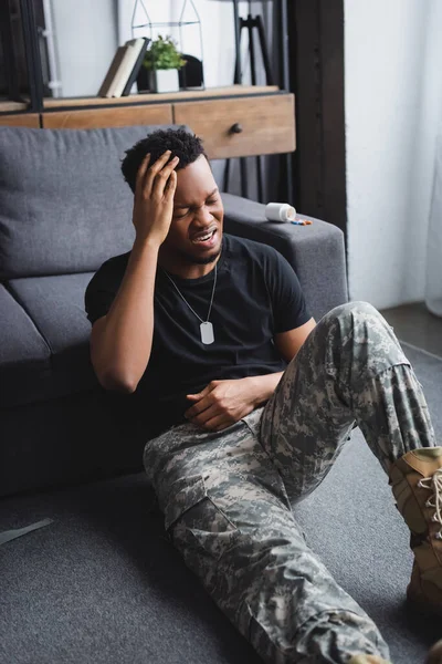 Crying african american soldier with army badge suffering from PTSD at home — Stock Photo