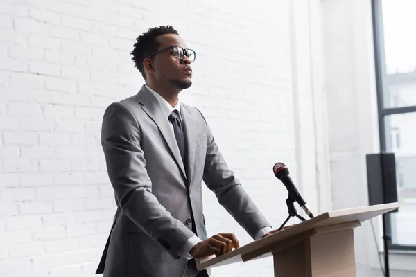 Confident african american business speaker standing on podium with microphone in conference hall — Stock Photo