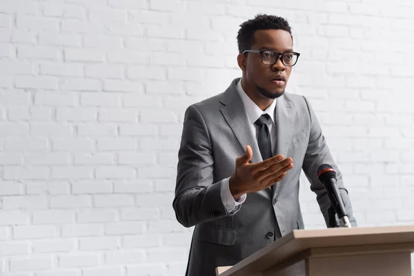 Confident african american business speaker on tribune with microphone in conference hall — Stock Photo