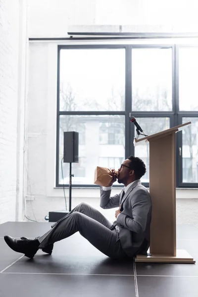 Stressed african american speaker breathing with paper bag and having panic attack during business conference in office — Stock Photo