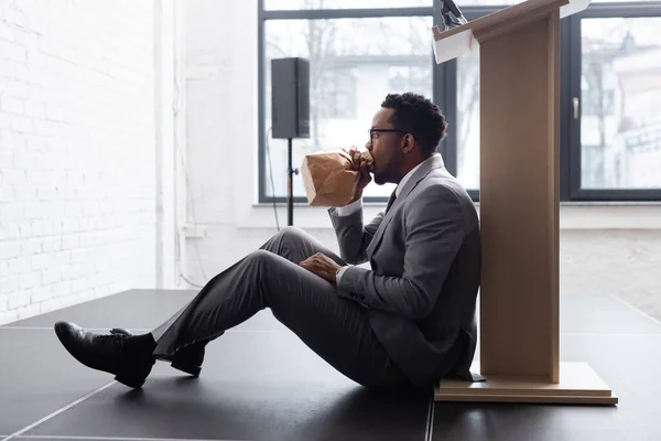 Nervoso afro-americano orador respirando com saco de papel e tendo ataque de pânico durante conferência de negócios no escritório — Fotografia de Stock