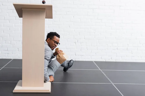 Scared african american speaker with paper bag having panic attack during business conference in office — Stock Photo