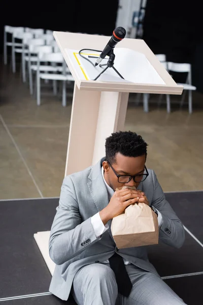 Falante afro-americano assustado respirando com saco de papel e tendo ataque de pânico antes da conferência de negócios — Fotografia de Stock