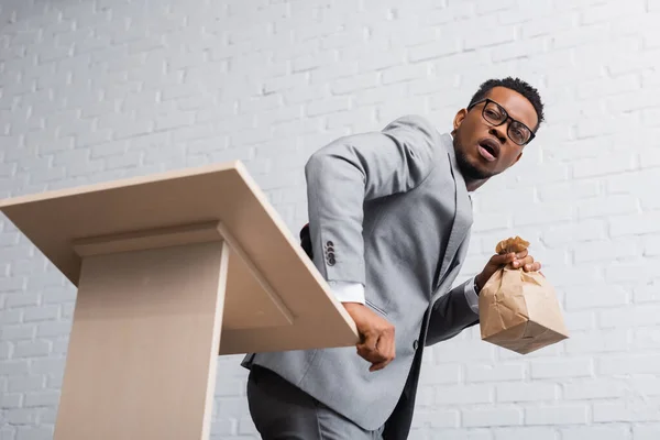 Scared african american speaker holding paper bag and having panic attack during business conference in office — Stock Photo