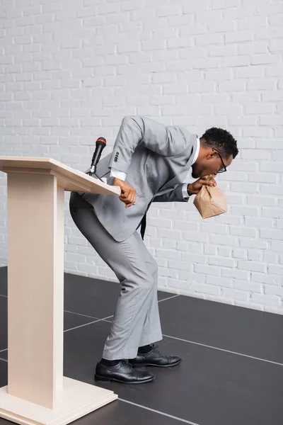 Stressed african american speaker breathing with paper bag and having panic attack on business conference — Stock Photo