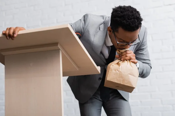 Homme d'affaires afro-américain nerveux respirant avec un sac en papier et ayant une crise de panique lors d'une conférence d'affaires au bureau — Photo de stock