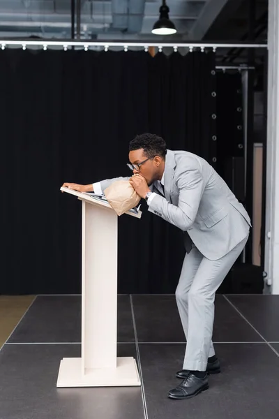 Souligné haut-parleur afro-américain respirant avec sac en papier et ayant une attaque de panique sur la conférence d'affaires — Photo de stock