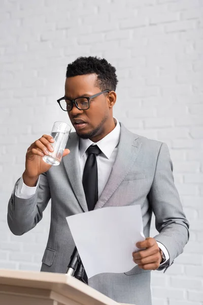 Nervous african american speaker holding paper and drinking water on business conference in office — Stock Photo
