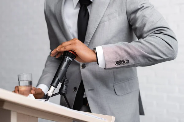 Vista ritagliata di altoparlante africano americano nervoso in possesso di un bicchiere d'acqua e microfono di copertura durante la conferenza di lavoro — Foto stock