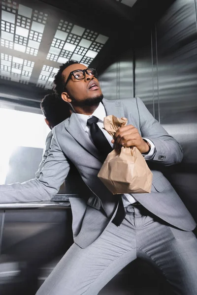 Homme d'affaires afro-américain effrayé avec sac en papier souffrant d'une attaque de panique dans l'ascenseur — Photo de stock