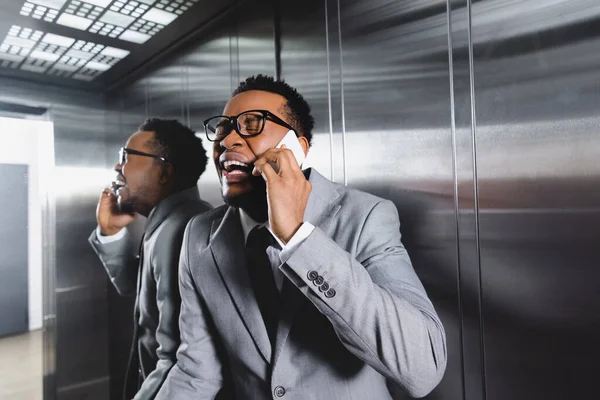 Crying african american businessman talking on smartphone and suffering from panic attack in elevator — Stock Photo