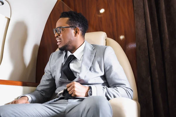 Nervous african american businessman holding safety belt and having panic attack during flight on private plane — Stock Photo