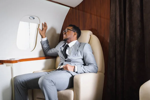 Nervioso afroamericano empresario sosteniendo cinturón de seguridad y sufriendo de ataque de pánico durante el vuelo en avión privado - foto de stock