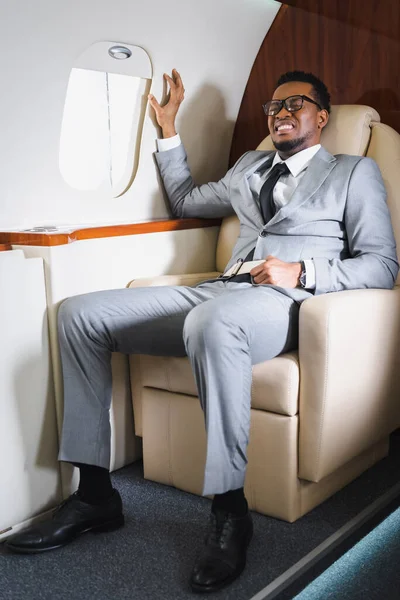 Homme d'affaires afro-américain tenant la ceinture de sécurité et souffrant d'une attaque de panique pendant le vol en avion privé — Photo de stock