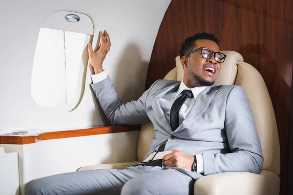 African american businessman holding safety belt and suffering from panic attack during flight on plane — Stock Photo