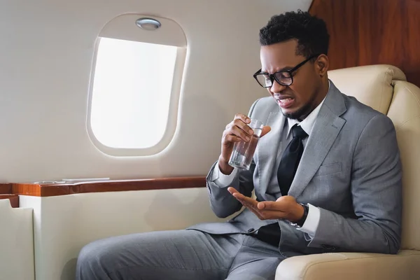Homme d'affaires afro-américain nerveux prenant des pilules tout en ayant une attaque de panique pendant le vol en avion privé — Photo de stock