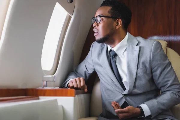 Nervöser afrikanisch-amerikanischer Geschäftsmann blickt durch Fenster und hat Panikattacke während Flug im Privatflugzeug — Stockfoto