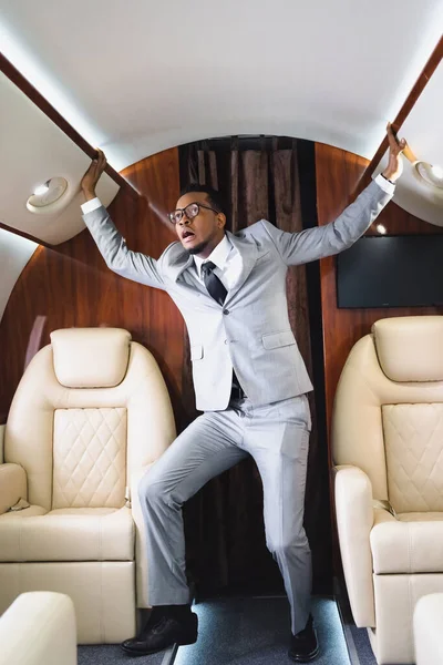 Scared african american businessman standing and having panic attack during flight on private plane — Stock Photo