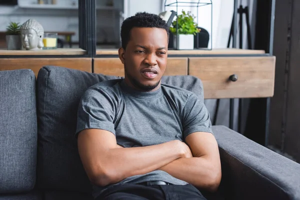 Depressed african american man sitting with crossed arms on sofa at home — Stock Photo