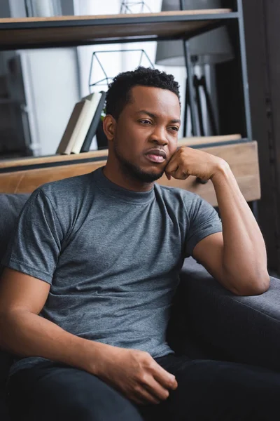 Sad african american man sitting on sofa at home — Stock Photo