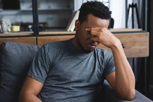 Homme afro-américain frustré assis sur le canapé à la maison — Photo de stock