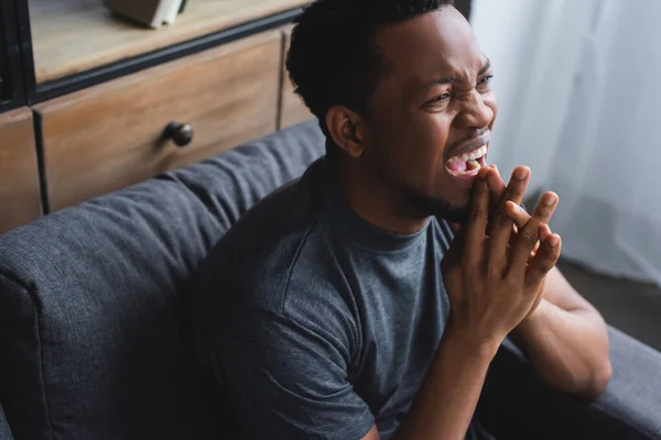 Homem afro-americano estressado gritando e sentado no sofá em casa — Fotografia de Stock