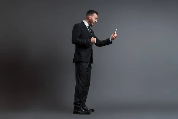 Profile of angry businessman in suit screaming while looking at smartphone on grey — Stock Photo